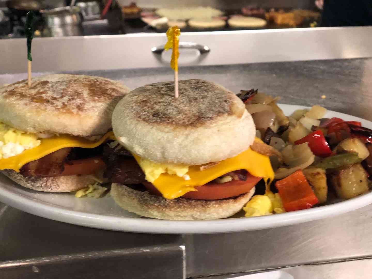 Toasted English muffin breakfast sandwich with American cheese, tomato, bacon & sausage