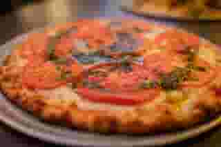 Pizza with sliced of tomato and pesto drizzled on top