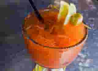 Michelada in a schooner glass with lemon and olive garnish and tajin rim.