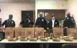 Five Laguna Beach police officers standing behind long table with brown Urth bags and lunch boxes