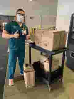 Male nurse with mask giving thumbs up standing next to a cart full of Urth food bags.