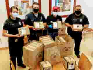3 police and one Urth employee standing at table loaded with Urth Caffé lunch boxes