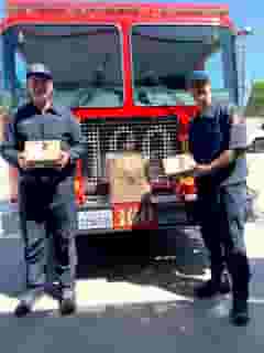2 firemen holding Urth lunch boxes standing in front of red firetruck fr