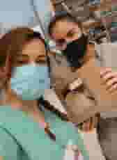 Two nurses upclose with masks, on is holding a lunch box from Urth Caffé.