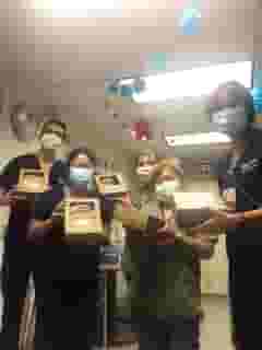 Group of five medical personel with masks in hallway all holding lunch boxes.