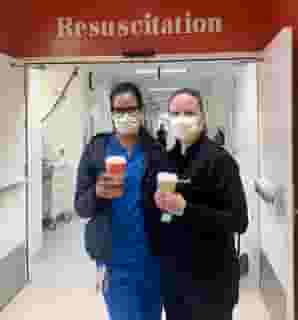 Two nurses with medical masks holding Urth Caffé To Go coffee cups. They are standing in front of open double doors with "Resuscitation" above them.