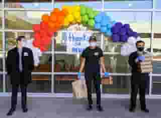 Three people standing in front of large glass window of St. Joseph's hospital with band of balloons and Urth Lunch boxes and bags.
