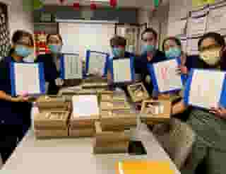 Six nurses with masks standing around table full of Urth lunch boxes each holding a large card with a letter on it together spelling T H A N K U.