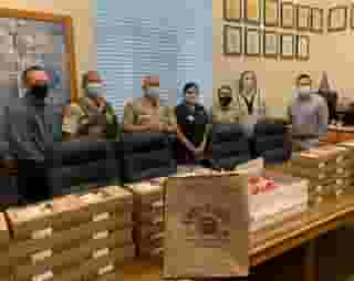 South Gate Police, 4 men, 3 women standing behind long table stacked 4 high with Urth lunch boxes