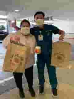 Male and female nurses with masks holding Urth food bags, coffee cup and giving thumbs up.