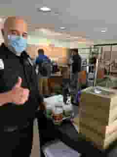 Security guard with mask standing next to cart of Urth lunch boxes and coffee cups giving thumbs up.