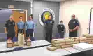Four City of Orange policemen with two Urth employees standing in front of City seal on wall and behind a table full of Urth lunch boxes and coffee