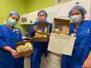 Three nurses in blue scrubs with masks holding open lunch boxes from Urth Caffé.