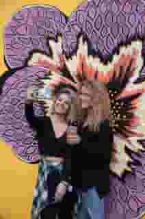 Two women in front of a purple and yellow flower mural