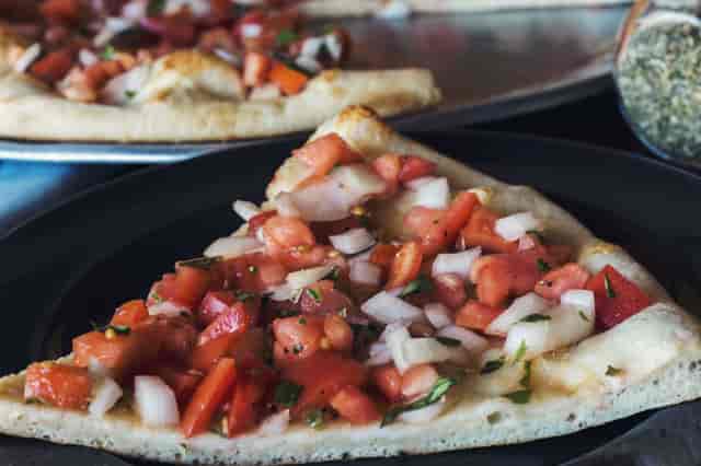 A slice of pizza with tomatos, onions, peppers and herbs.