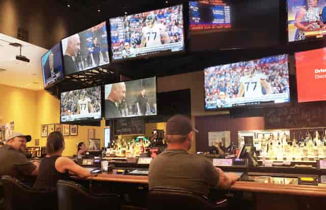 Patrons sitting at a bar with many big screen TVs
