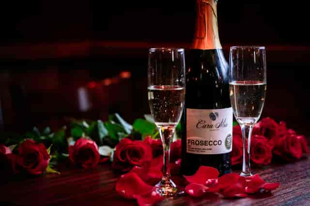a bottle of sparkling wine with 2 glasses and roses