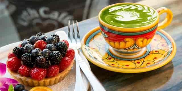 Fruit tart and cup of green tea latte with bird design