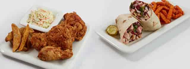 plate of wings, fries, and coleslaw next to a plate with a wrap and sweet potato fries