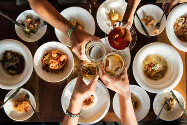 Multiple dishes on a table with a group toasting with various drinks