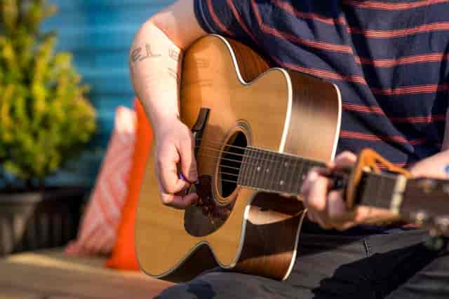 Man in a striped shirt strumming an accoustic gutar.