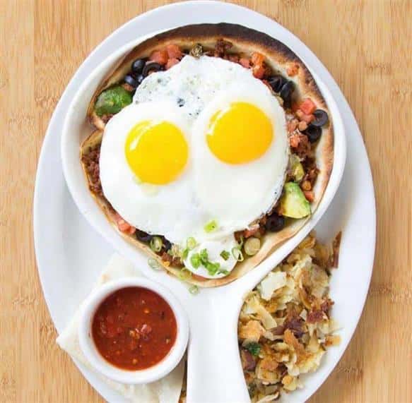 Breakfast bowl topped with two sunny-side up eggs with a side of home fries and salsa	