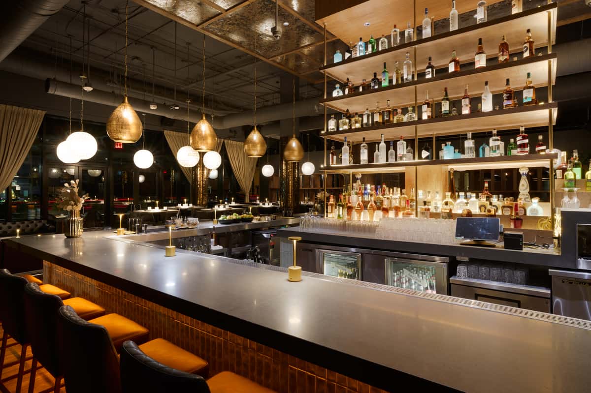 A chic bar at Fitoor featuring a sleek countertop, stylish seating, and illuminated shelves stocked with a variety of spirits, creating a sophisticated ambiance for guests.