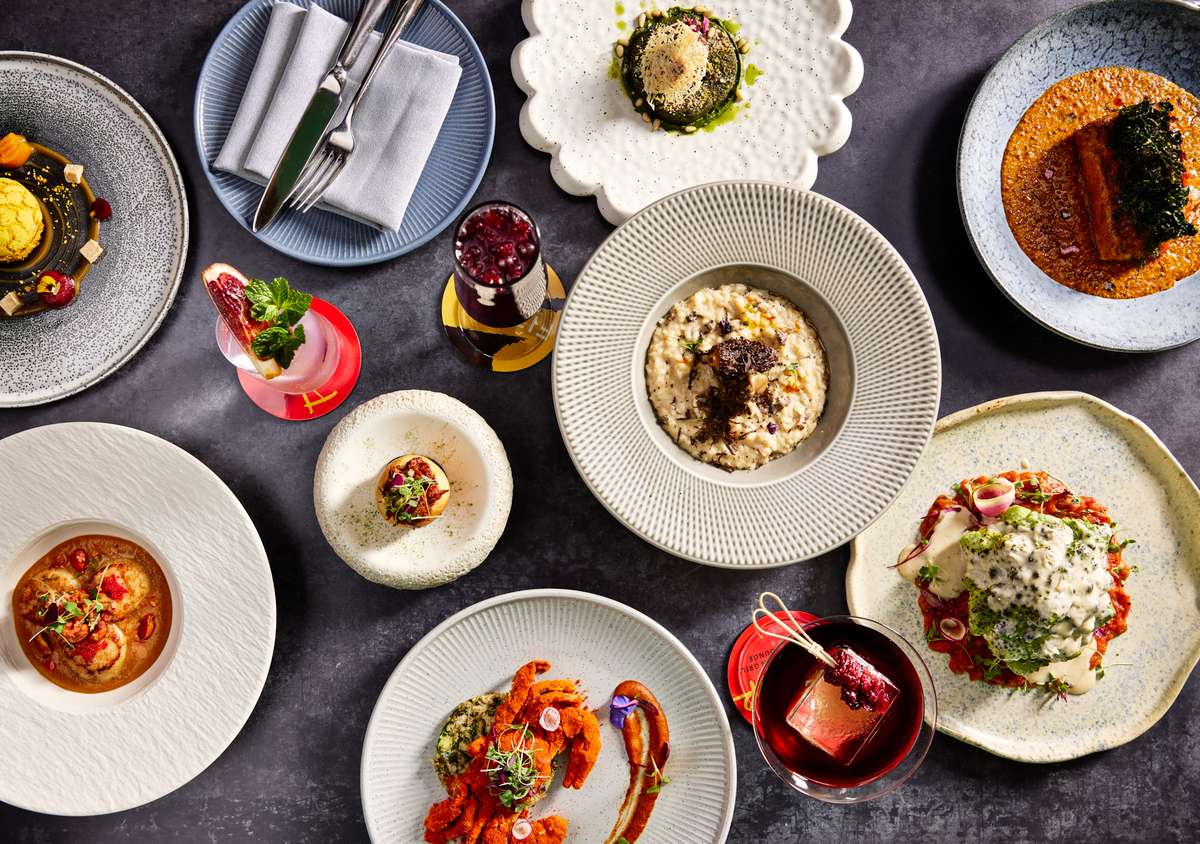 An overhead view of a vibrant spread at Fitoor Indian Grill & Lounge, showcasing diverse Indian dishes, colorful garnishes, and elegant drinks on stylish plates.