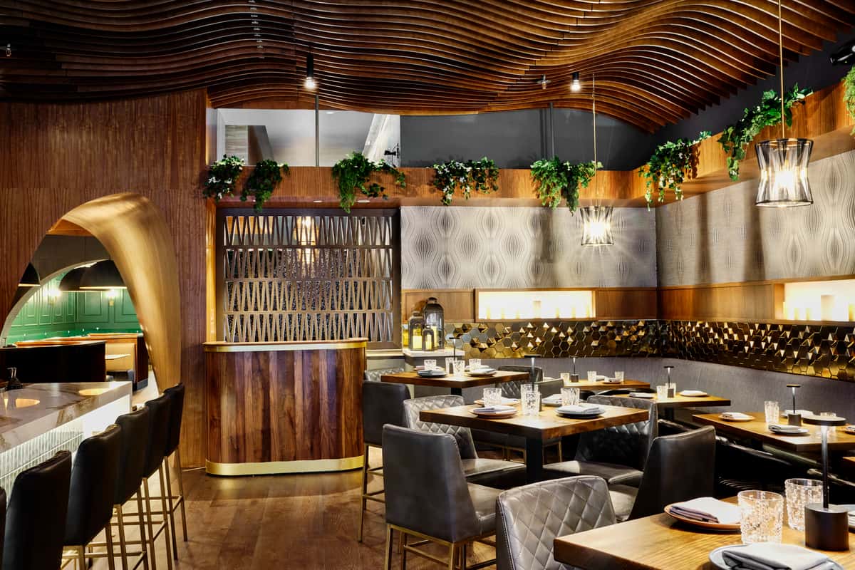 The interior of FITOOR Indian Grill & Lounge in San Jose, CA, features elegant wooden decor, stylish seating, and ambient lighting, creating a warm and inviting dining atmosphere.