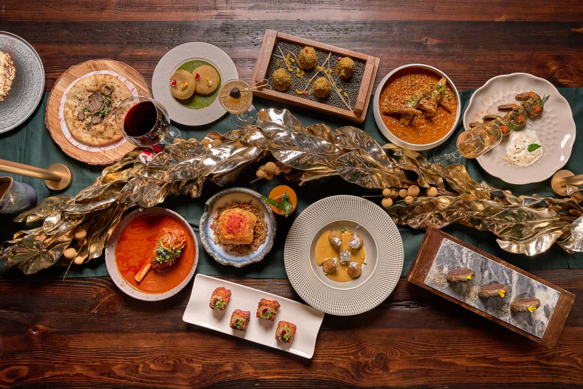 An elegant spread of Indian dishes at Fitoor Santa Monica, featuring vibrant curries, appetizers, and desserts, beautifully arranged on a wooden table, showcasing culinary artistry.