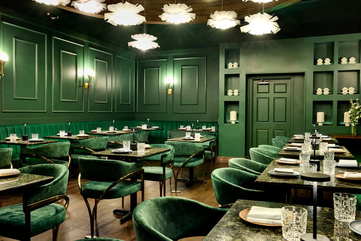 An elegant private event space featuring deep green walls and plush seating, with stylish tables set for dining, illuminated by unique light fixtures, perfect for intimate gatherings.