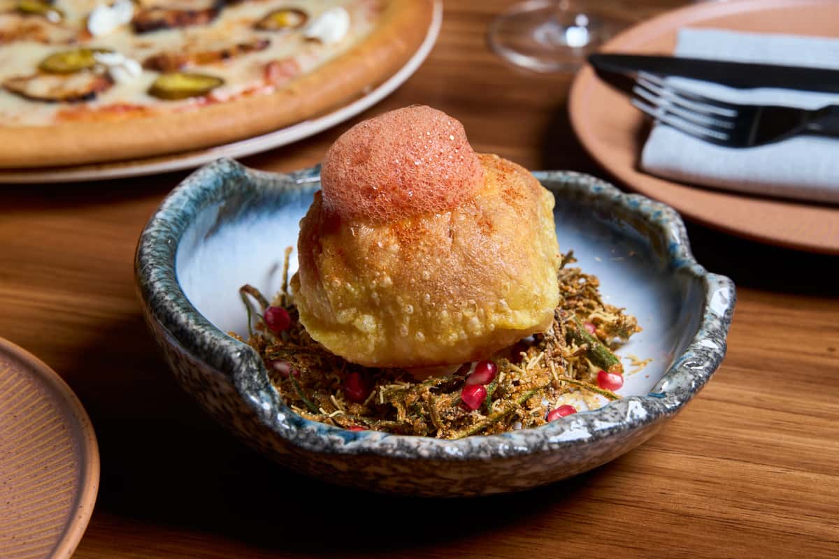 A vibrant dish featuring a crispy, hollow puri filled with flavorful ingredients, topped with a frothy garnish, served on a bed of crunchy garnishes, perfect for online ordering.