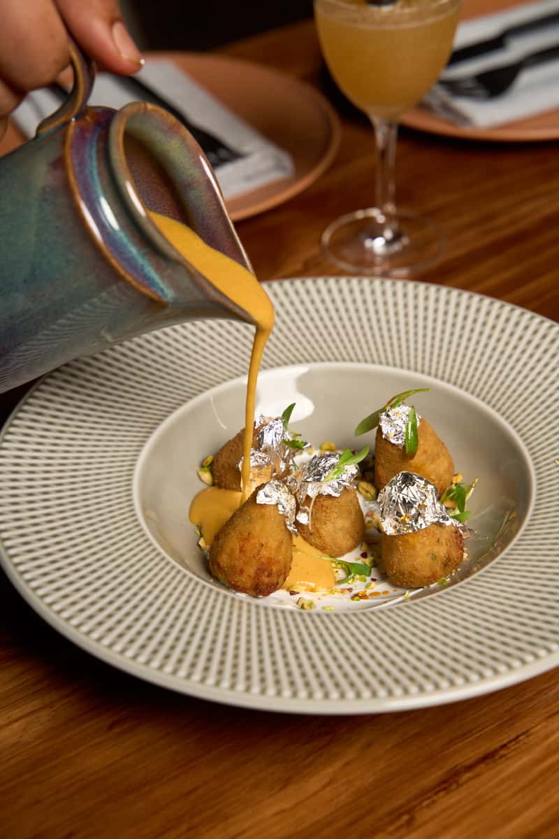 Golden croquettes with edible silver foil resting in a creamy sauce, garnished with fresh herbs, beautifully plated to emphasize gourmet Indian culinary artistry
