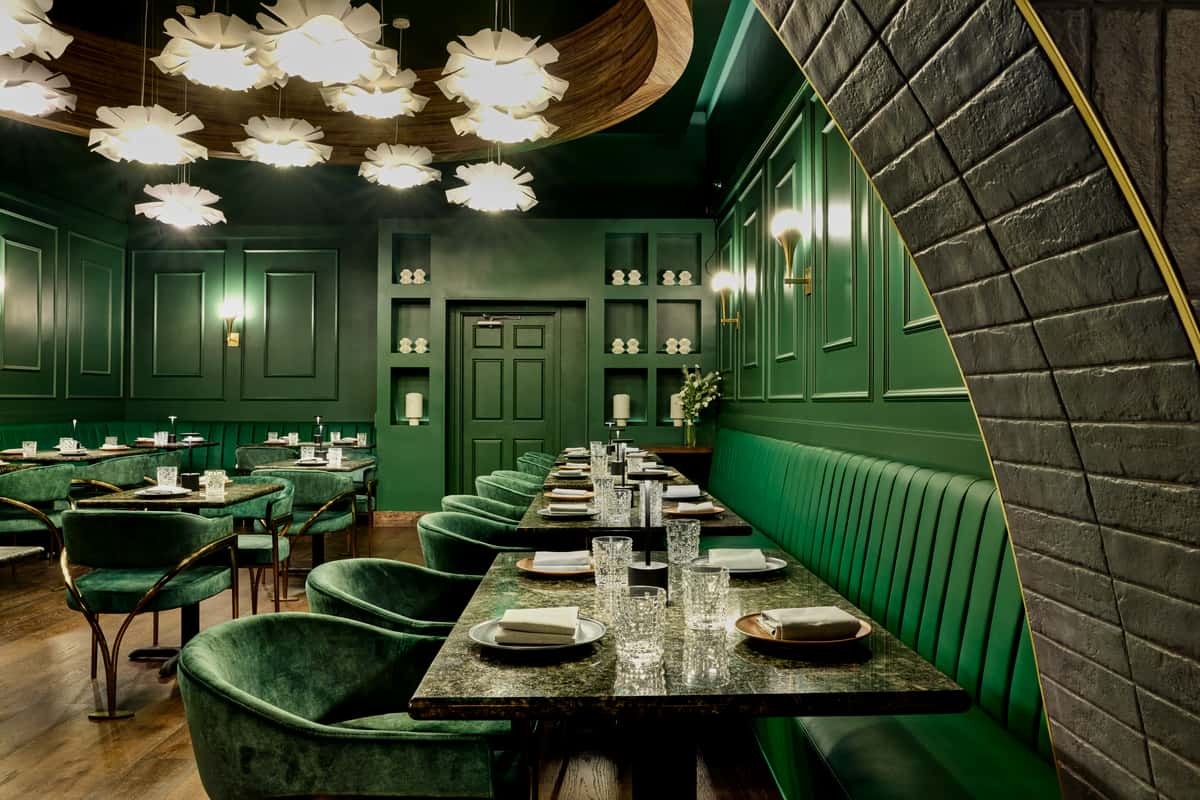 The chic interior of FITOOR Indian Grill & Lounge in Santa Monica features deep green walls, elegant seating, and stylish lighting, creating a sophisticated dining atmosphere.