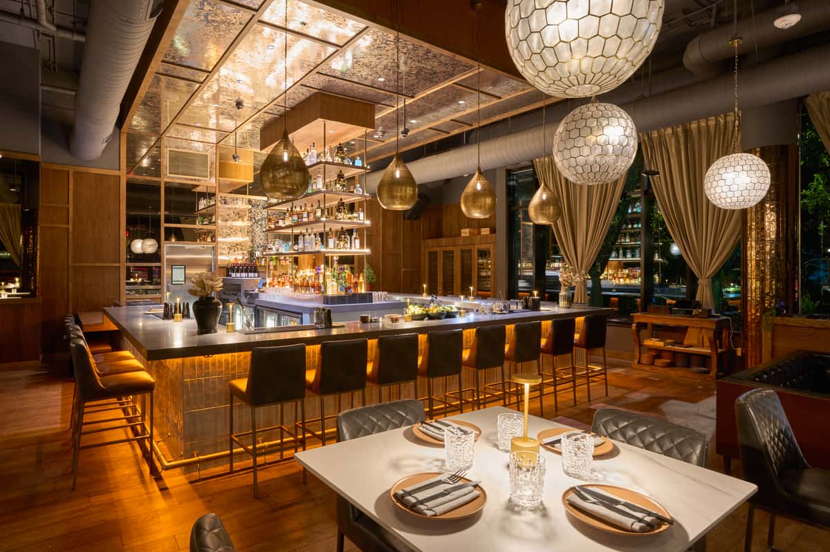 A stylish interior featuring a modern bar with illuminated shelves, elegant seating, and decorative lighting, creating a warm and inviting atmosphere for dining and socializing.