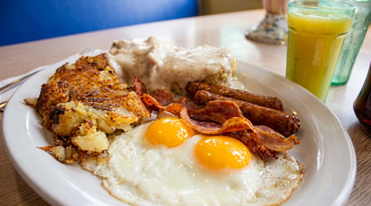 Hearty breakfast platter featuring sunny-side-up eggs, crispy bacon, sausage links, and golden breakfast potatoes.