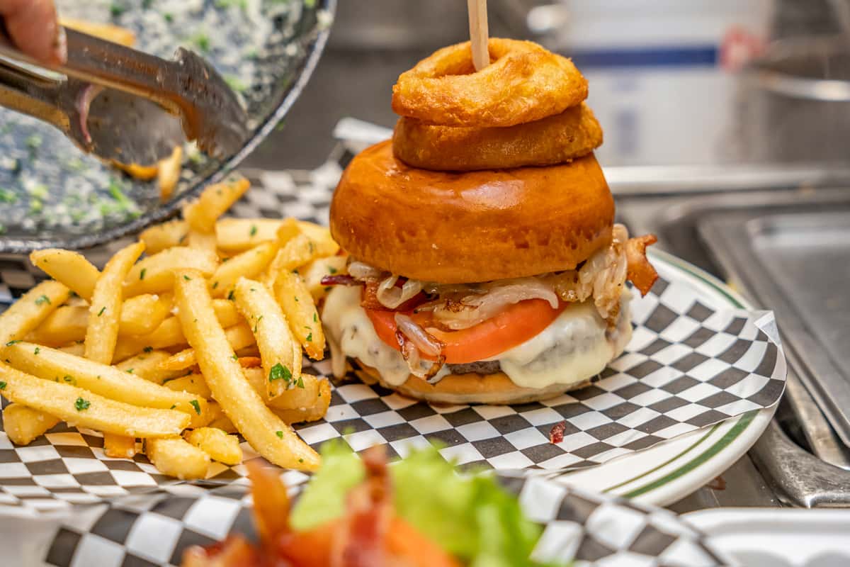Burger with onion rings on top with fries on the side