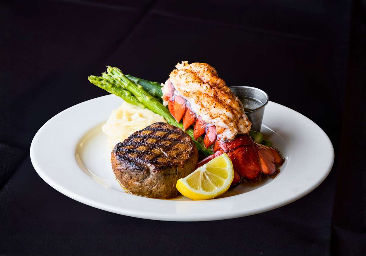 Grilled filet mignon and lobster tail served with asparagus, lemon, and drawn butter on a white plate.