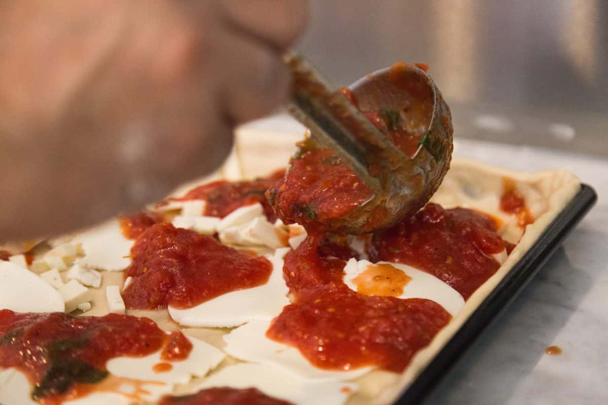 hand spreading pizza sauce