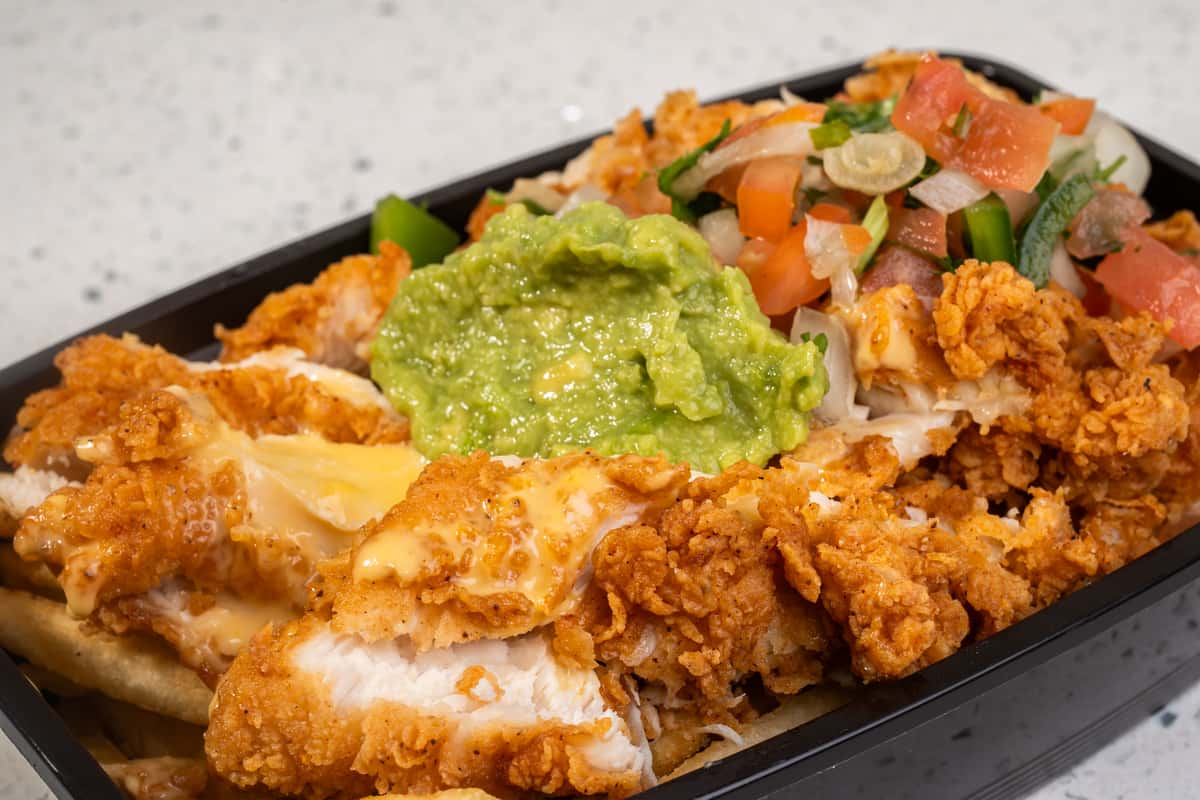Close-up of loaded fries topped with crispy chicken, cheese, vegetables, and guacamole.