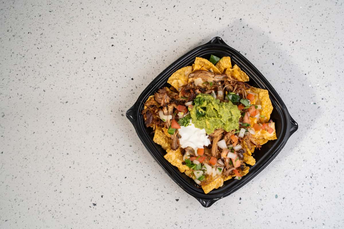 Overhead view of loaded nachos topped with meat, cheese, vegetables, sour cream, and guacamole.