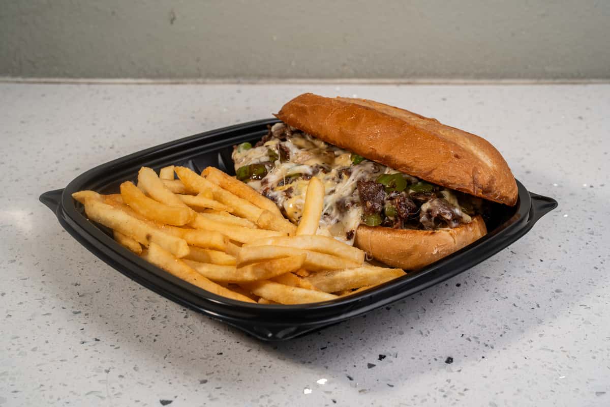 Philly cheesesteak sandwich served with french fries in a black takeout tray.