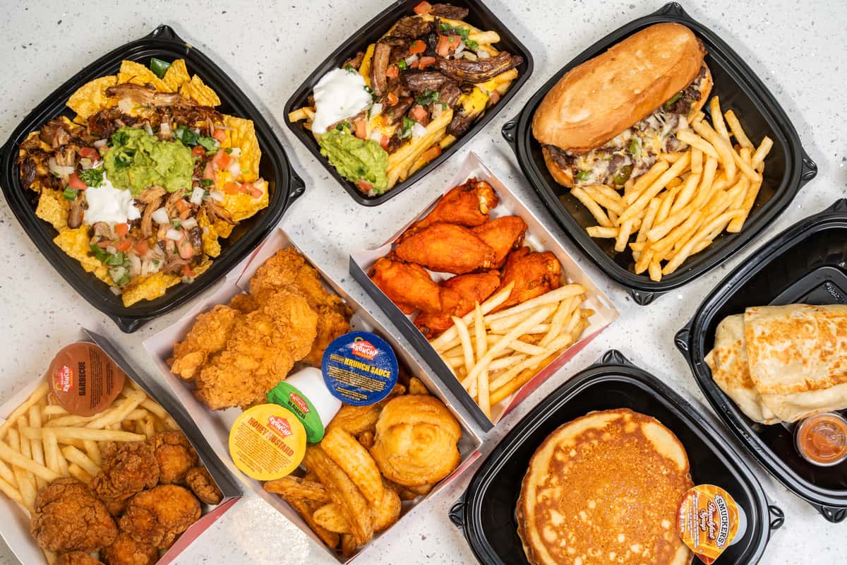 Overhead spread of loaded nachos, burgers, fries, wings, burritos, pancakes, and dipping sauces.