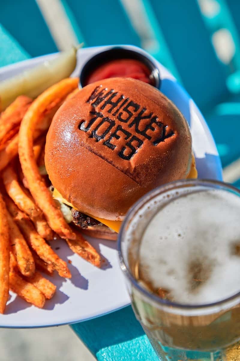 a close up of a burger served with fries and a cold beer