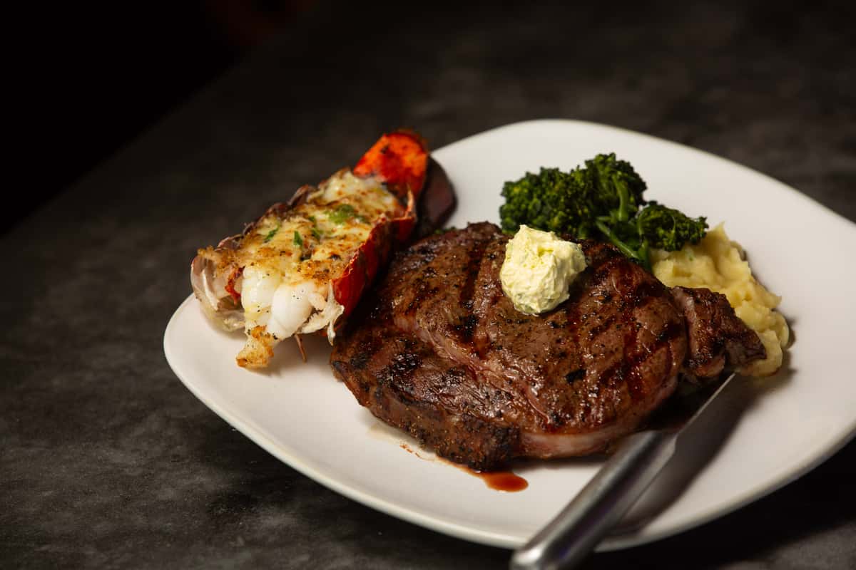 Grilled ribeye steak and broiled lobster tail served with mashed potatoes and broccolini at an upscale waterfront restaurant