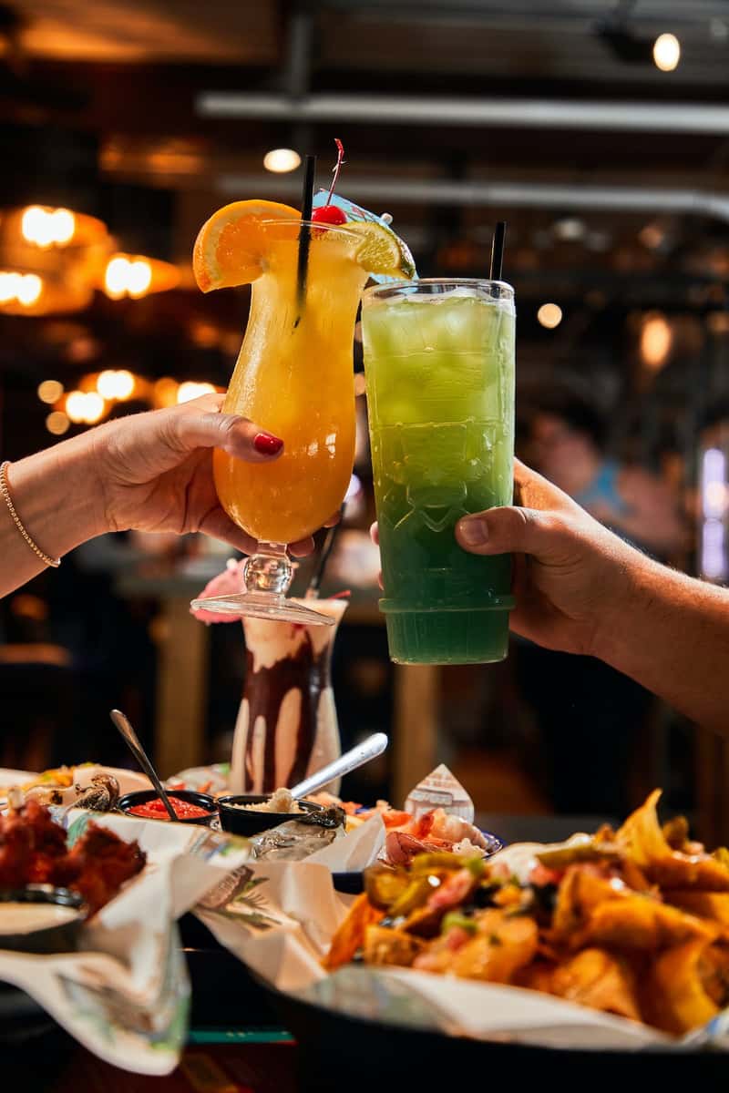 two people clicking their drink glasses together over a few plates of food