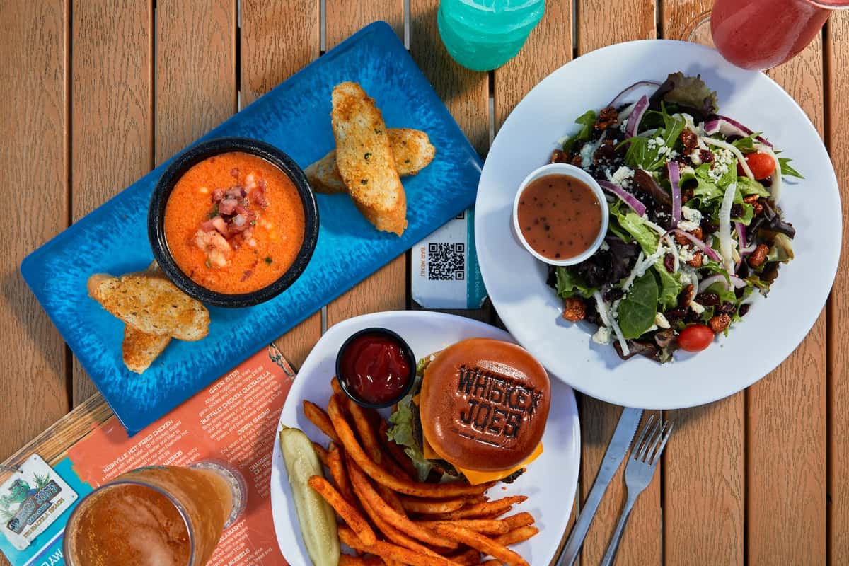 overhead shot of a burger, salad, and soup served on a wooden table