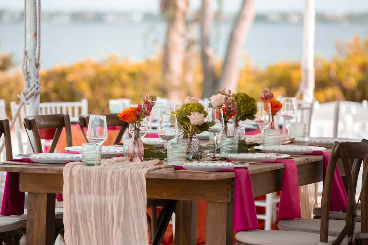 Rustic waterfront wedding reception table with colorful floral centerpieces, elegant place settings, and bayfront views