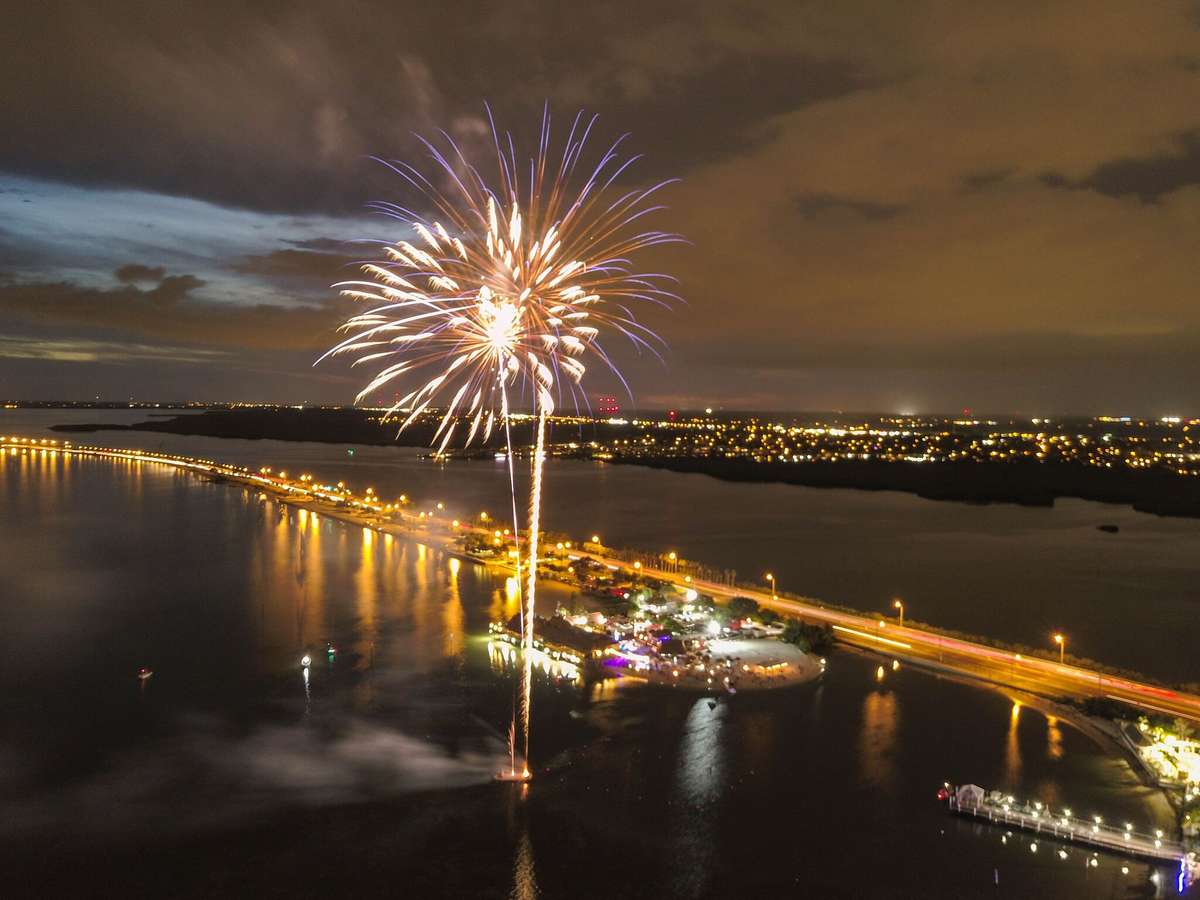 Aerial view of waterfront fireworks display over the bay and bridge at night near Whiskey Joe's beachside venue