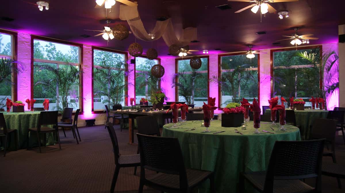 an event space decorated with green table cloths and pink lighting